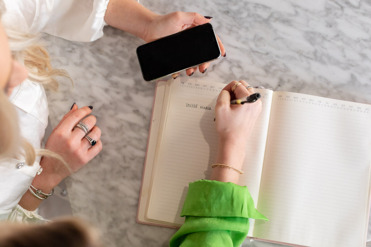 two women sitting together writing in a notebook planning out marketing services