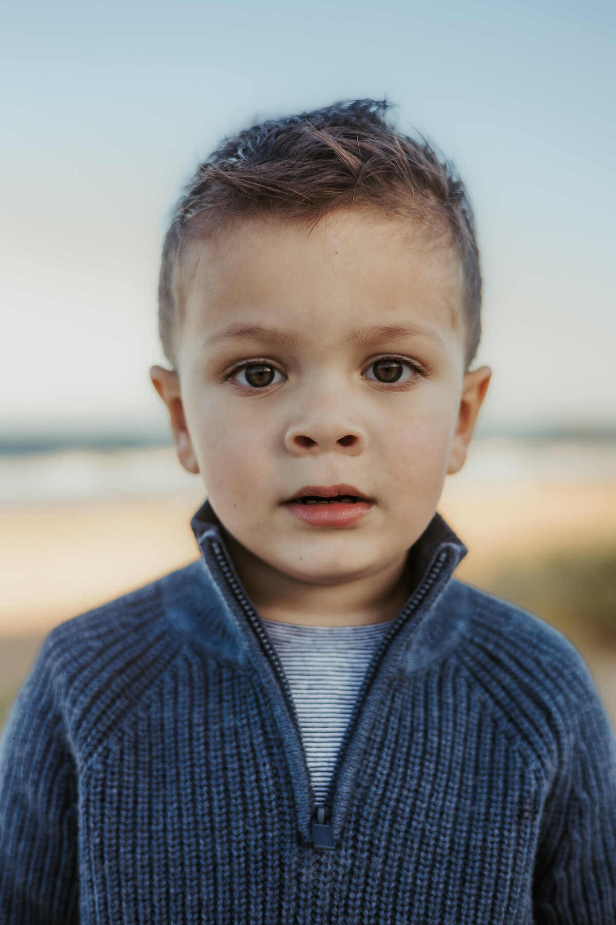 Two year old in a blue knit stares straight into the camera.