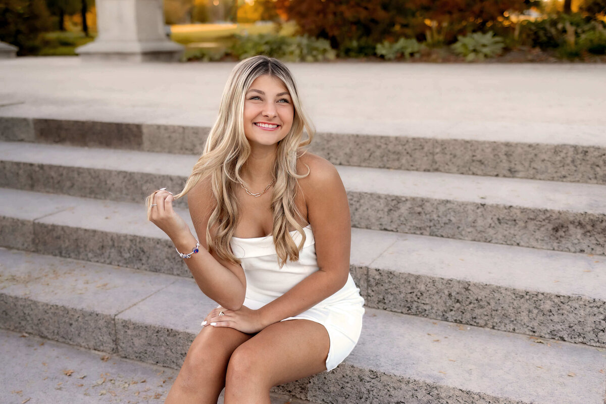 A beautiful blonde haired  girl is sitting on the steps ofthe Grand Basin in forrest park while Foppiano Photography captures her smiles.