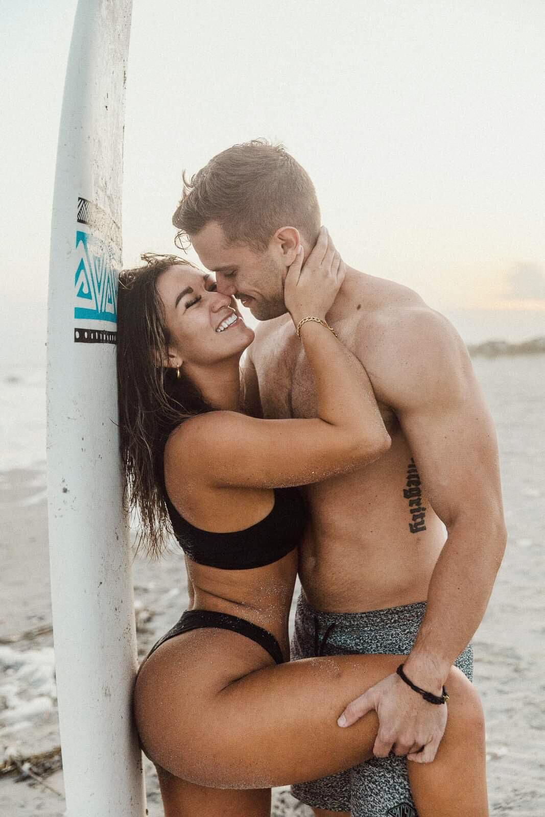 couple kissing against a surfboard pose