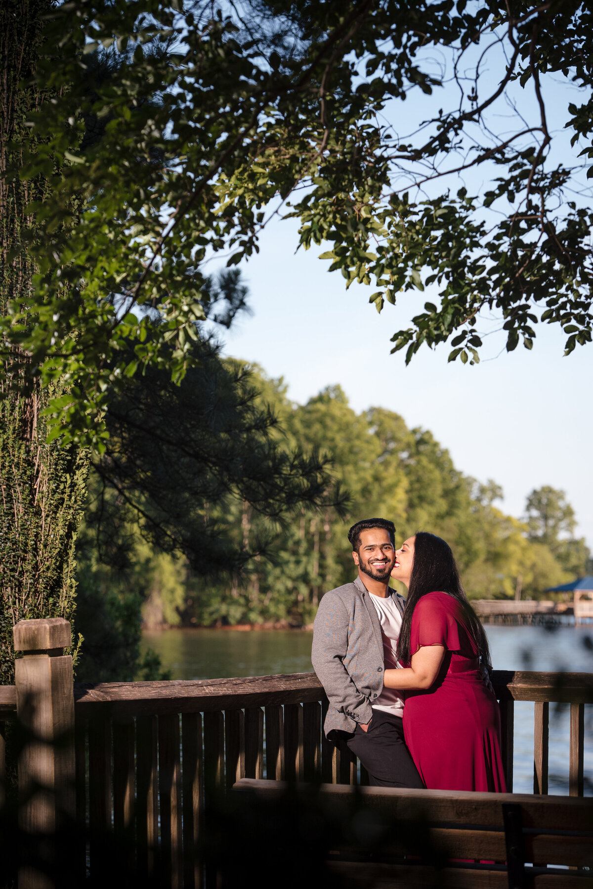 Indian-woman-kissing-Indian-man-on-his-cheek-with-greenery-and-a-lake-in-the-background-at-Jetton-Park