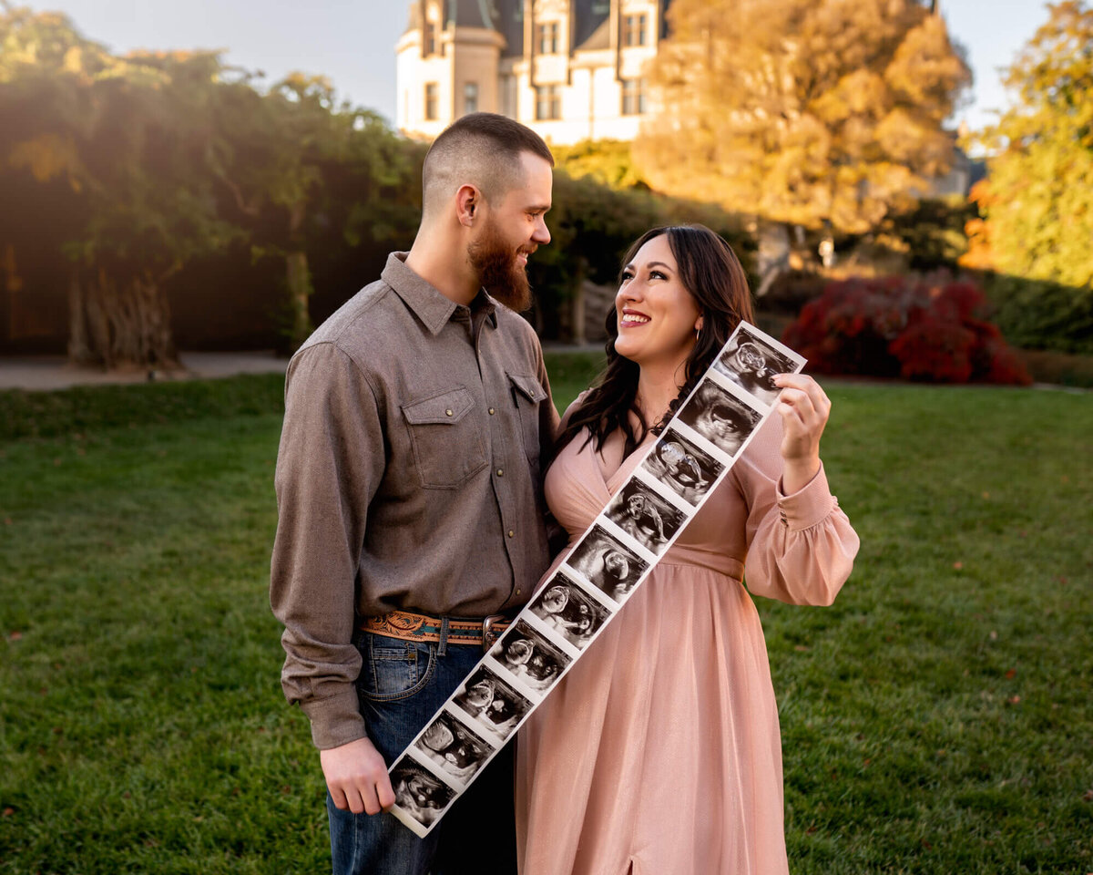 An adorable expecting couple hold up their sonogram photos while gazing into each others yes