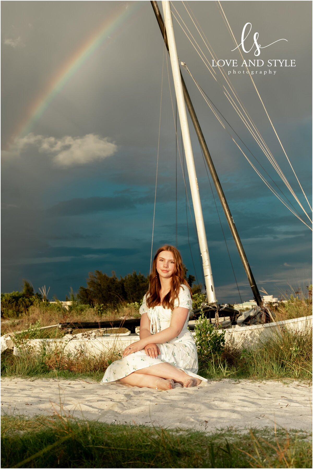 High school senior photo at Siesta Key beach with mini catamaran and rainbow behind her