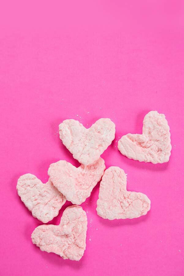 Pink heart-shaped marshmallows on a bright pink background.