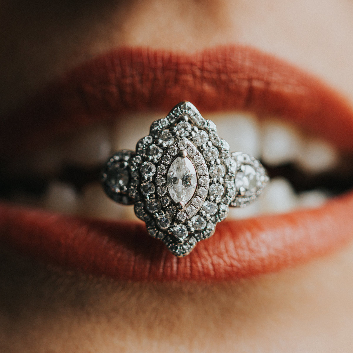 One of the top wedding photos of 2020. Taken by Adore Wedding Photography- Toledo, Ohio Wedding Photographers. This photo is of a custom engagement ring clenched between the brides teeth and red lips. The award winning wedding photo was taken in Toledo Ohio