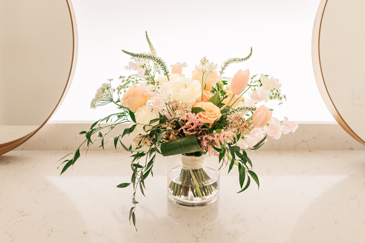 Pink and blush spring flowers in a wedding bouquet in a bridal suite next to two gold mirrors by JoLynn Photography