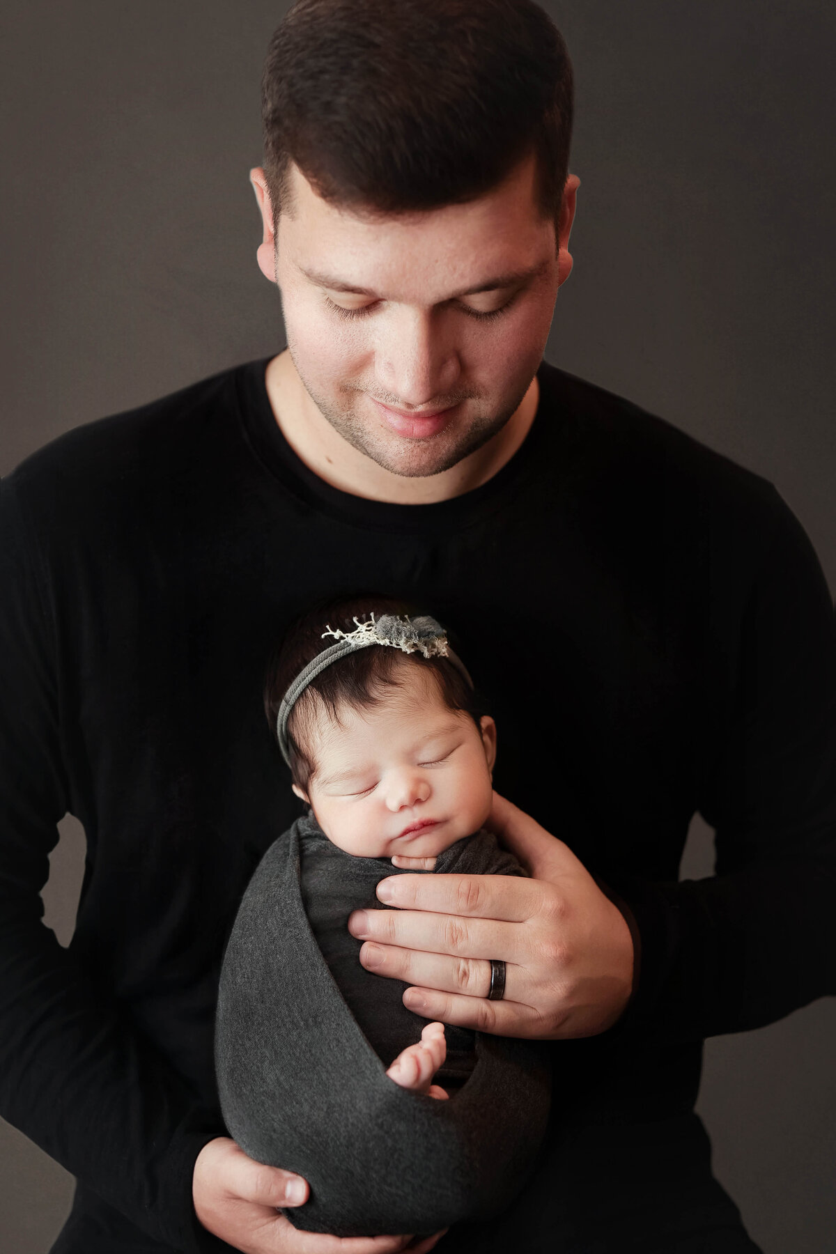 dad in black holding newborn girl while smiling