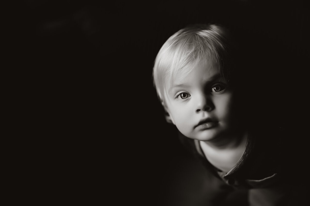 a window lit dramatic black and white portrait of a toddler looking directly at the camera