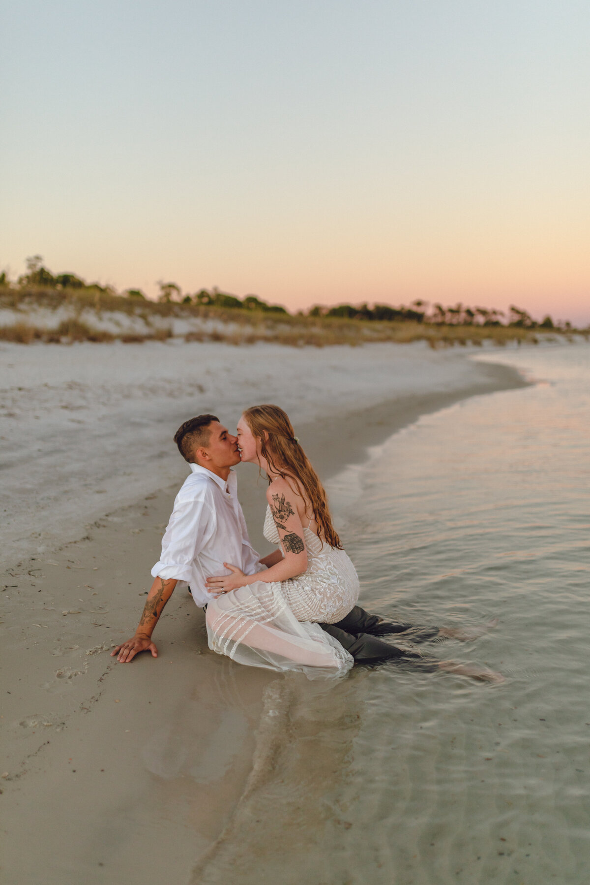 newlyweds kiss and she straddles him on edge of water in Panama City Beach after intimate wedding