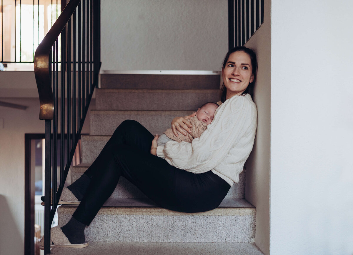 Mutter, welche ihr neugeborenes Baby im Arm hält und auf Treppe sitzt
