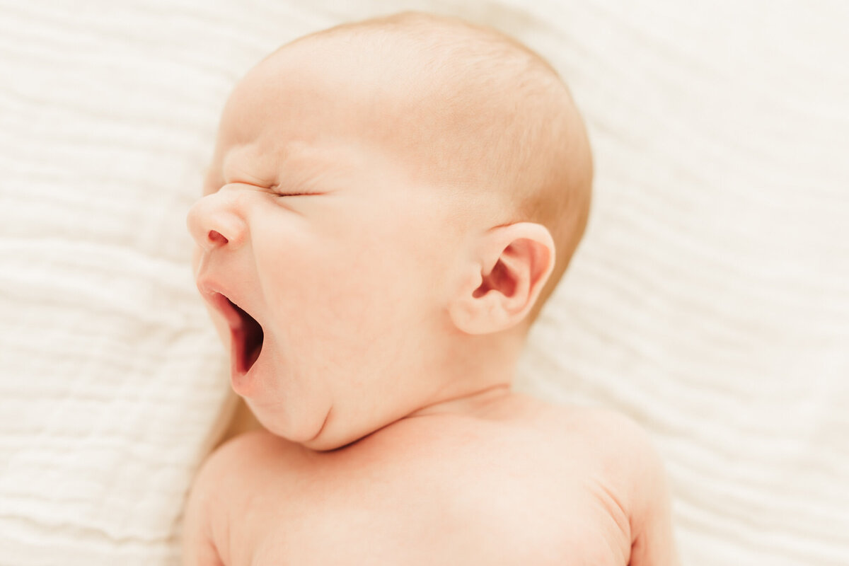 newborn yawning while laying on white blanket.