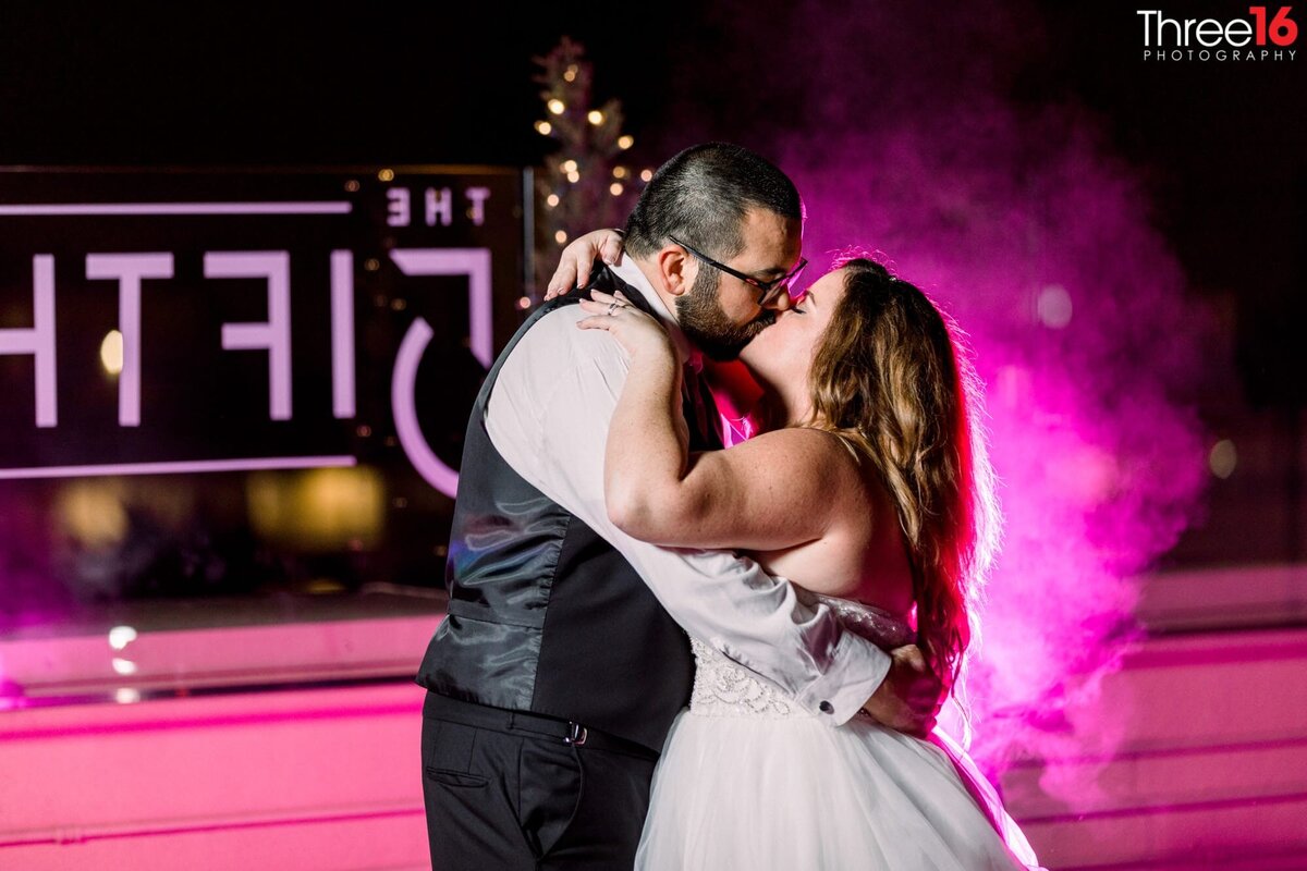 Bride and Groom share a quiet kiss with a pink haze in the background