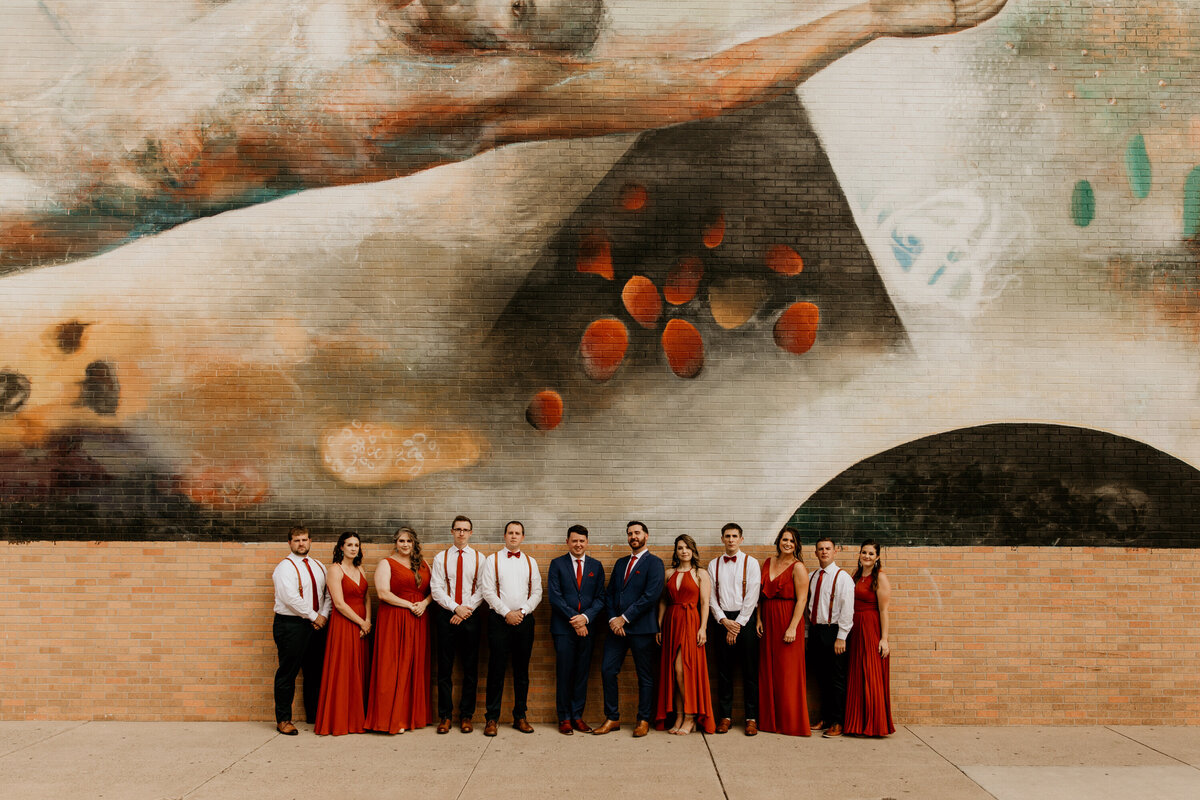 same sex couple and wedding party standing in front of an art wall downtown