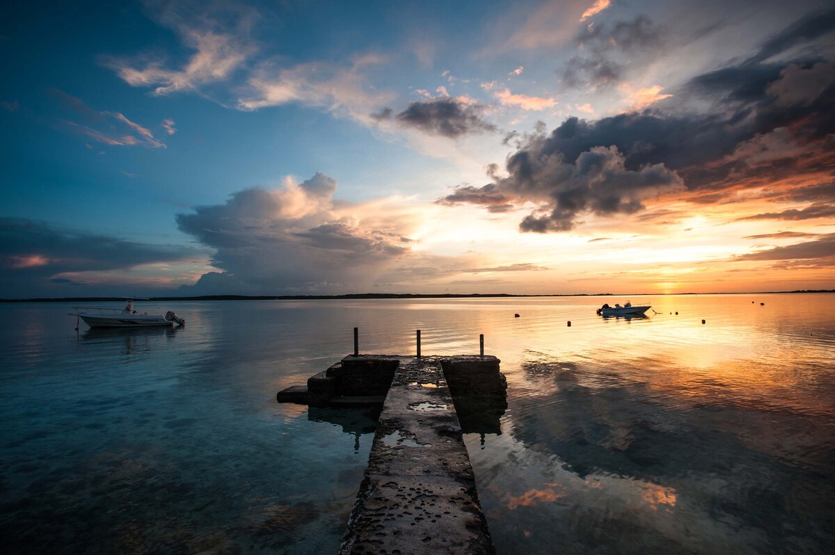 An old dock juts out into water at sunset. Tourism board marketing image