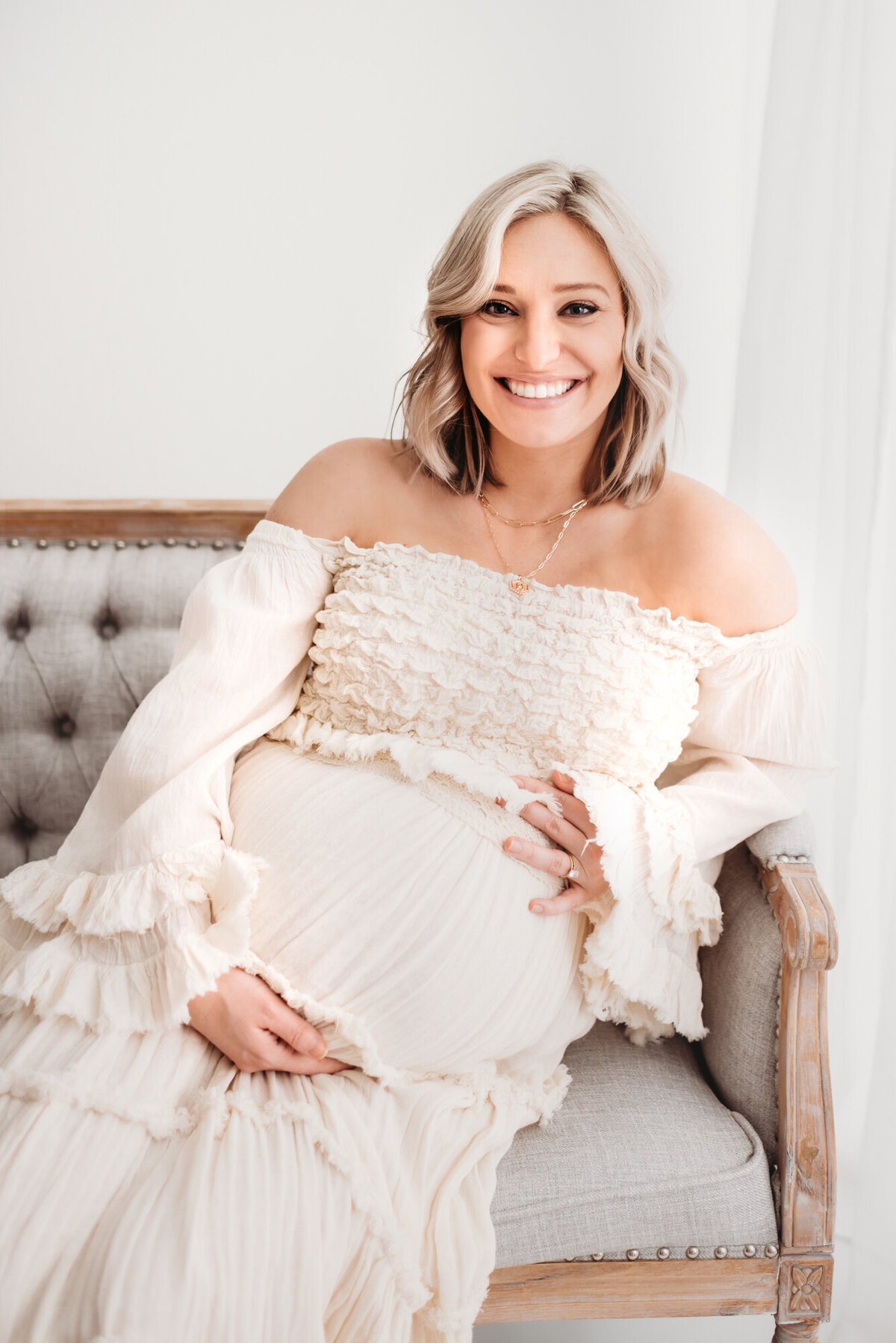 pregnant woman smiling at camera and holding her belly in white studio