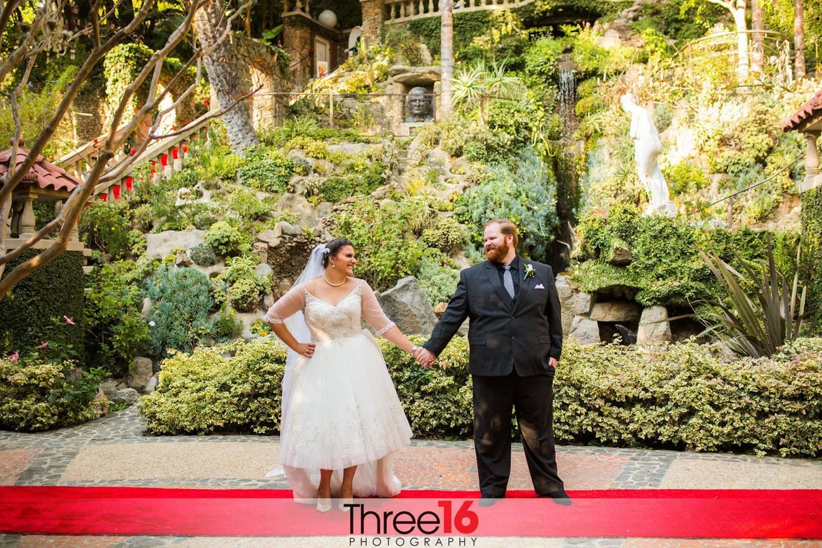 Newly married couple look at each other while holding hands on the red carpet aisle at the Houdini Estates wedding venue
