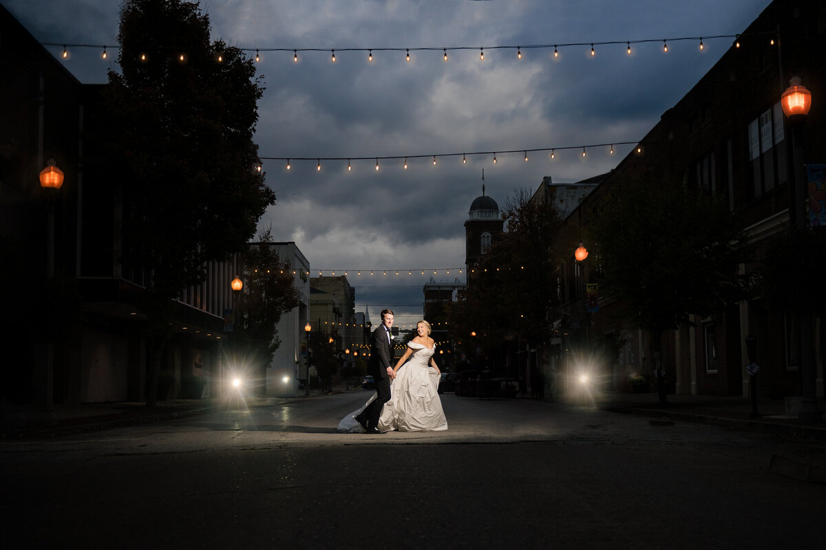 bride and groom hold hands run across crosswalk in street at night