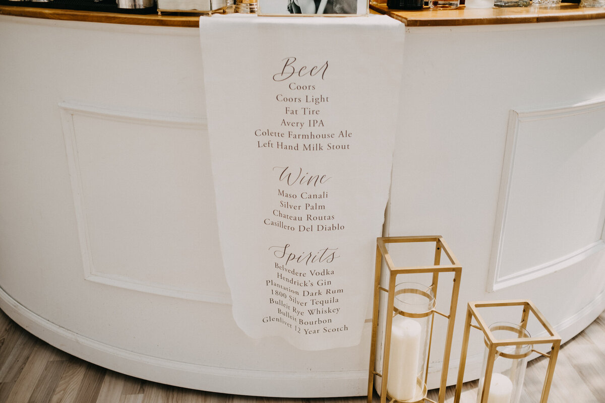 White fabric bar sign draped over white bar, with custom calligraphy design