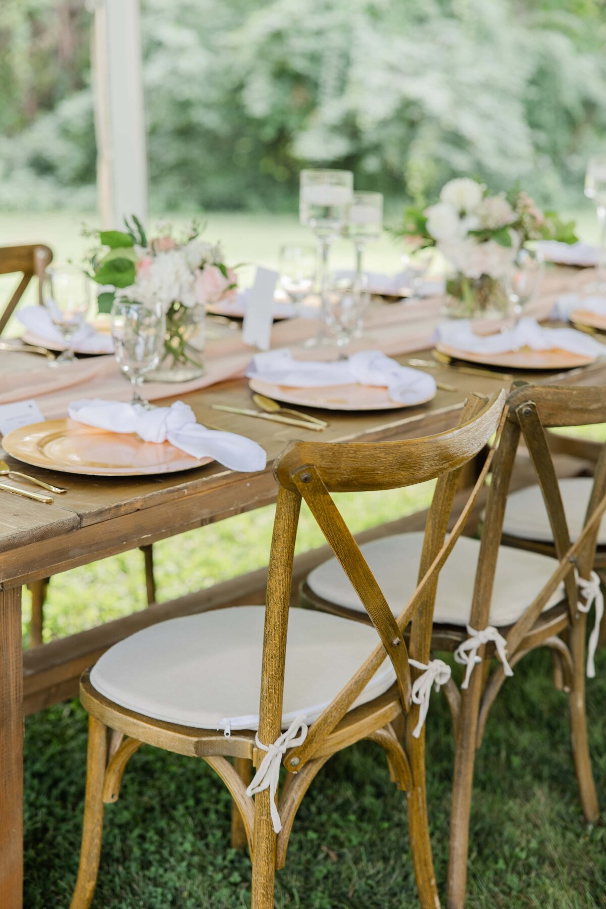 Elegant outdoor wedding table setup with wooden chairs, floral centerpieces, and fine dining ware on a lush green lawn at an Iowa park farm.