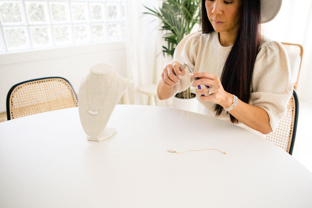 woman working on a necklace while sitting at table