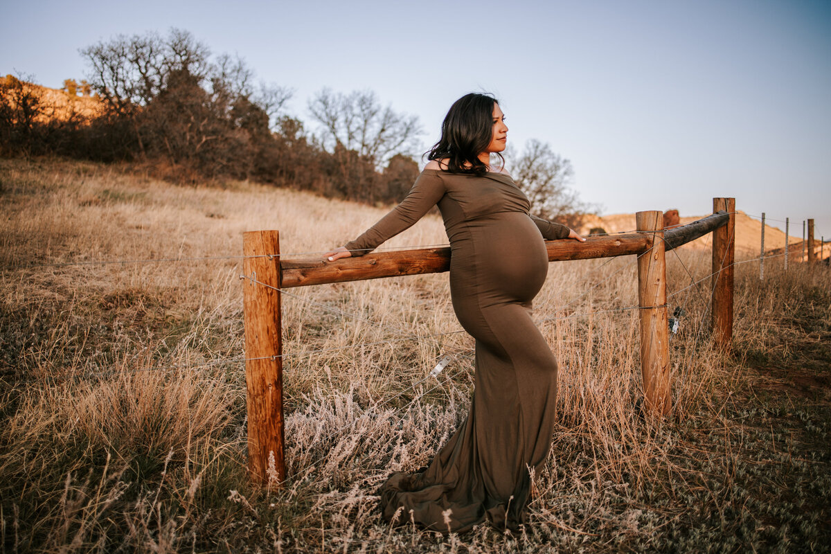 pregnant moms wear a  tight green dress against a fence for maternity photos