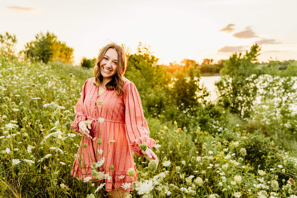 beautiful senior girl in a pink dress playing with queen anne's lace at sunset