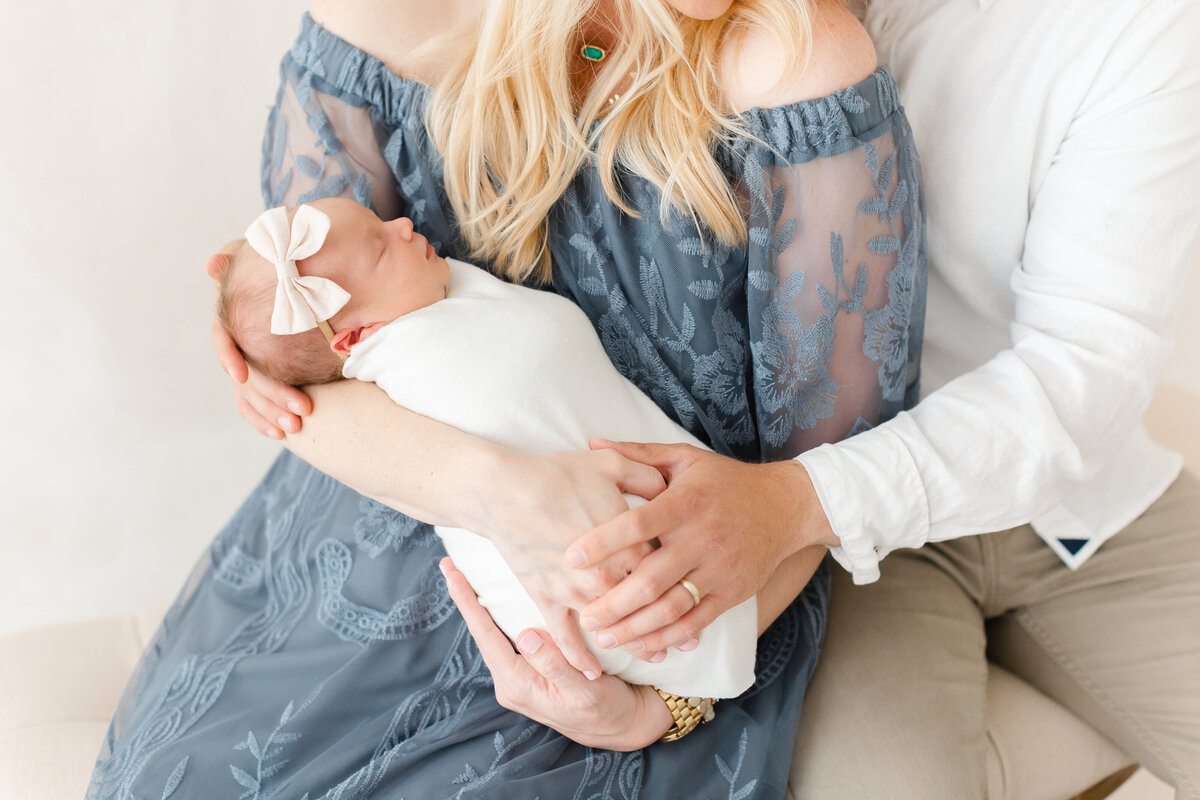 A closeup photo of a baby being held by her mother and father in front of a hand-painted canvas backdrop by Washington DC Family Photographer