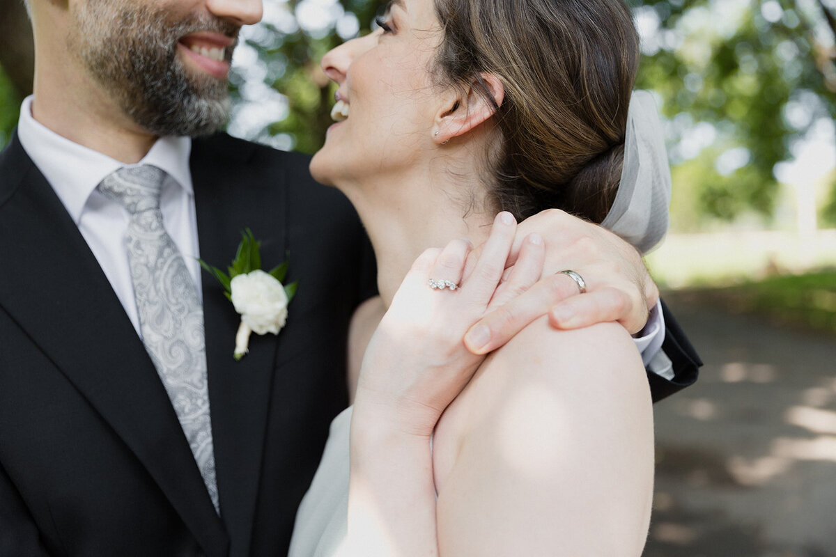 close up of couple laughing with holding fingers and focus is on wedding rings.