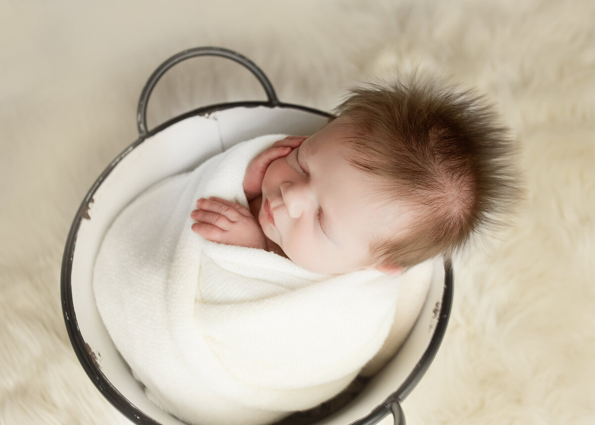Newborn baby boy wrapped in tan wrap sleeping in bucket during newborn session in Franklin Tennessee photography studio