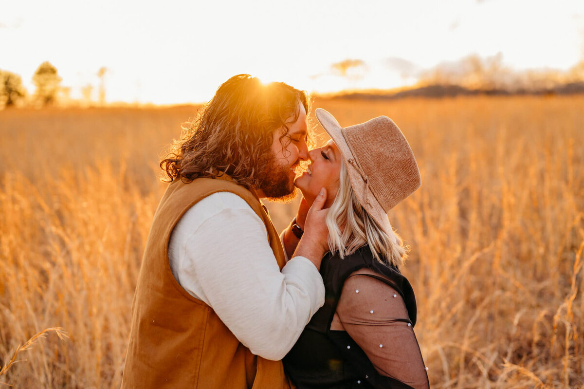 photo of a man caressing a woman's face as they kiss in a field at sunset