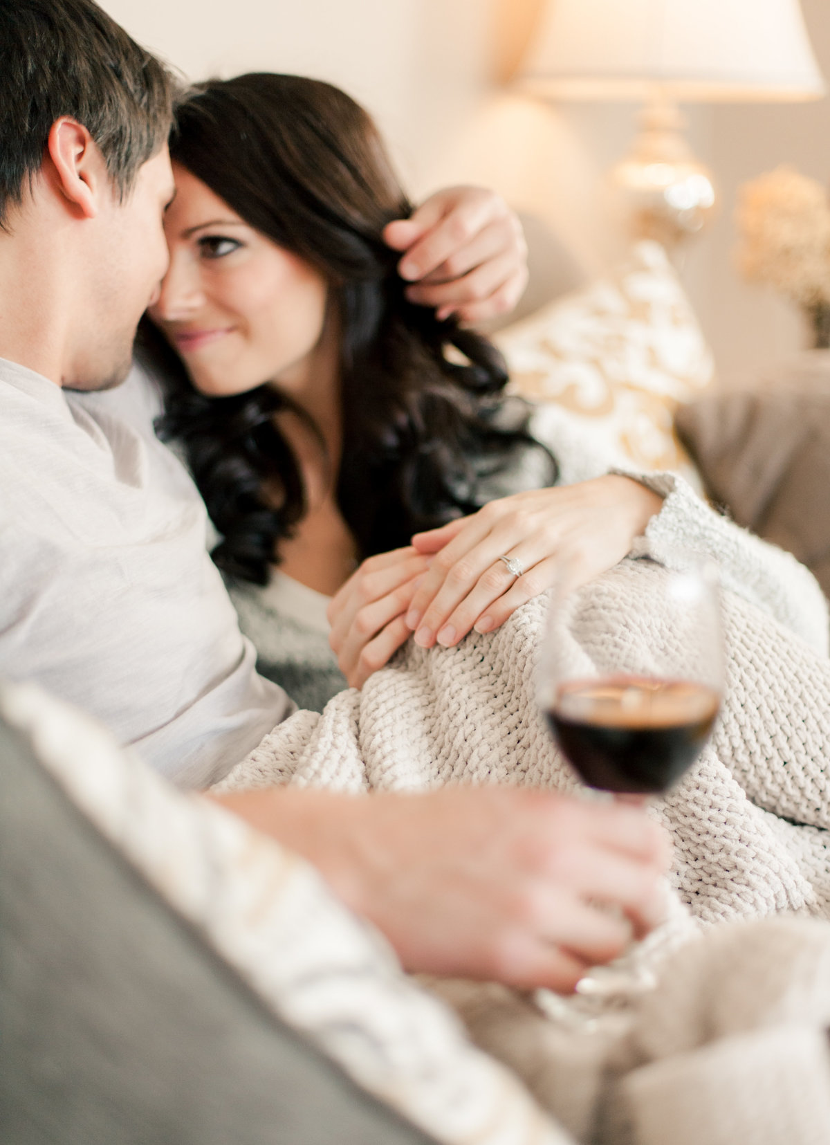 fiances hold wine and cuddle on the couch in rochester minnesota home for engagement photography