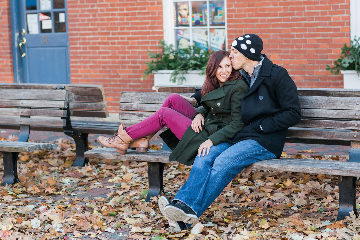 Fall and bricks serve as a backdrop for this kissing couple on a bench in Newburyport MA