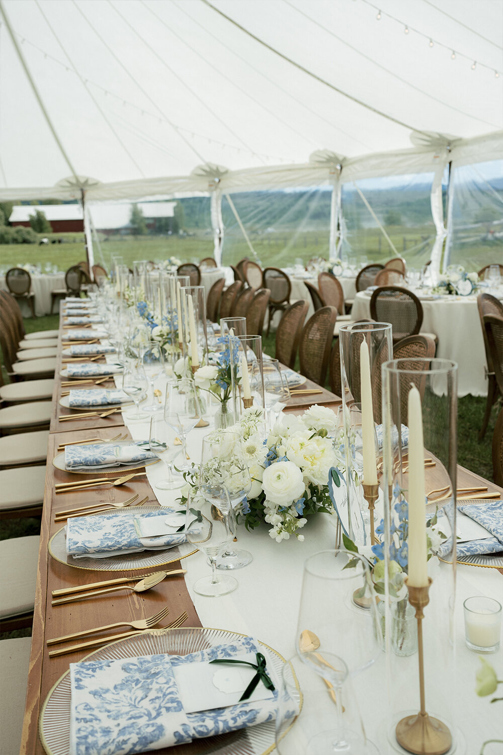 Summer wedding table place setting featuring a crisp white linen runner, soft candlelight, and fresh blue and white floral arrangements.