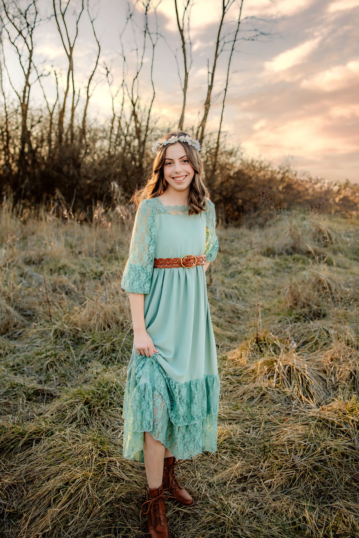 beautiful young lady in a long green dress in a field at sunset