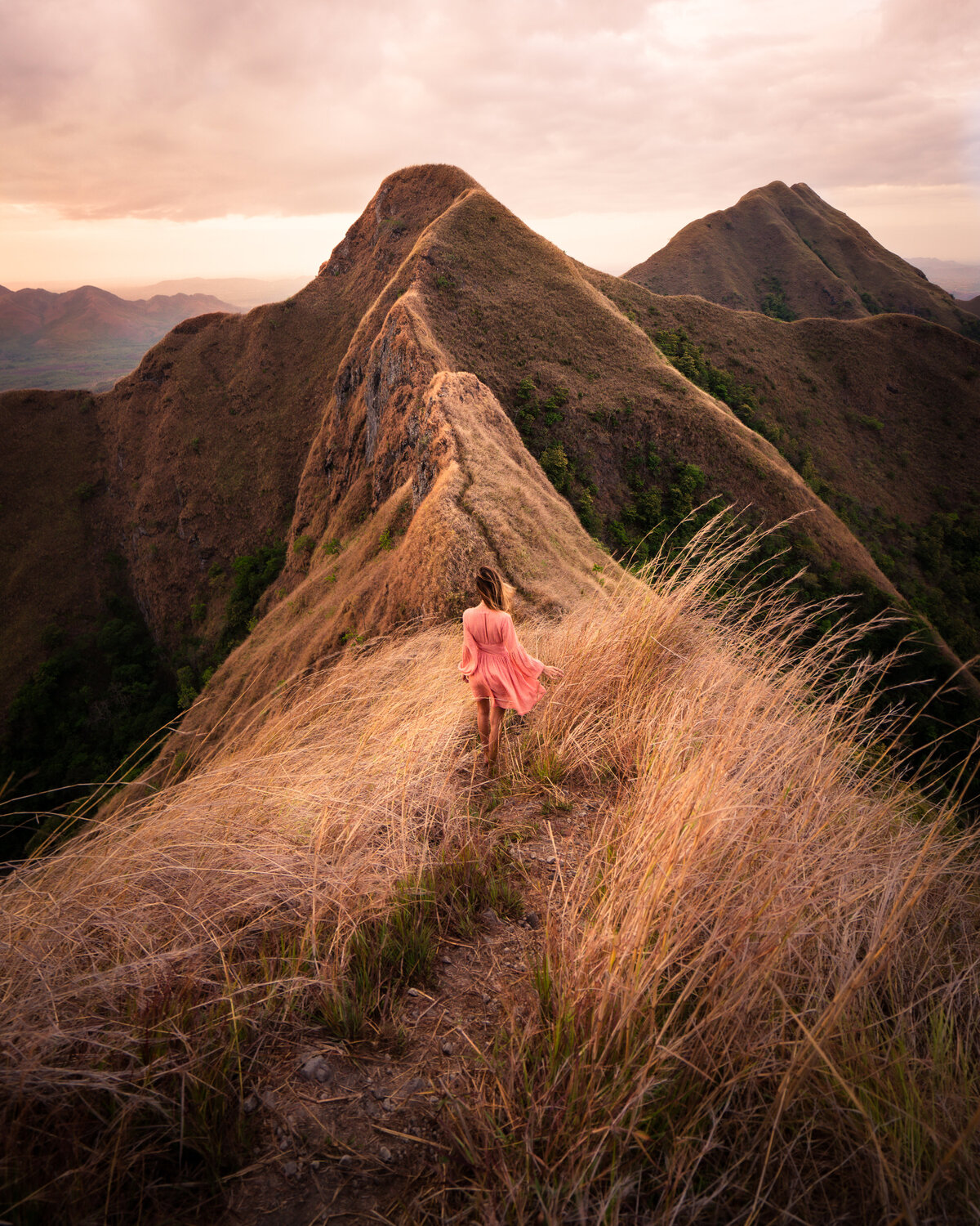 Jess of Jess Wandering in a pink dress walking through orange grass at the top of a mountain range