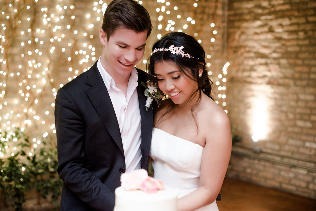 A smiling couple looking down at their wedding cake
