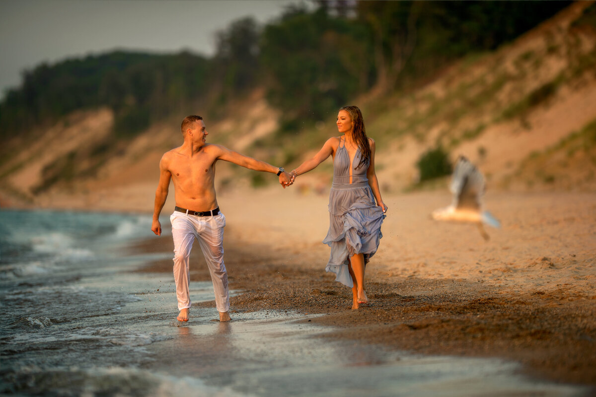 Engaged couple wet from the water  holding hands and running on the beach