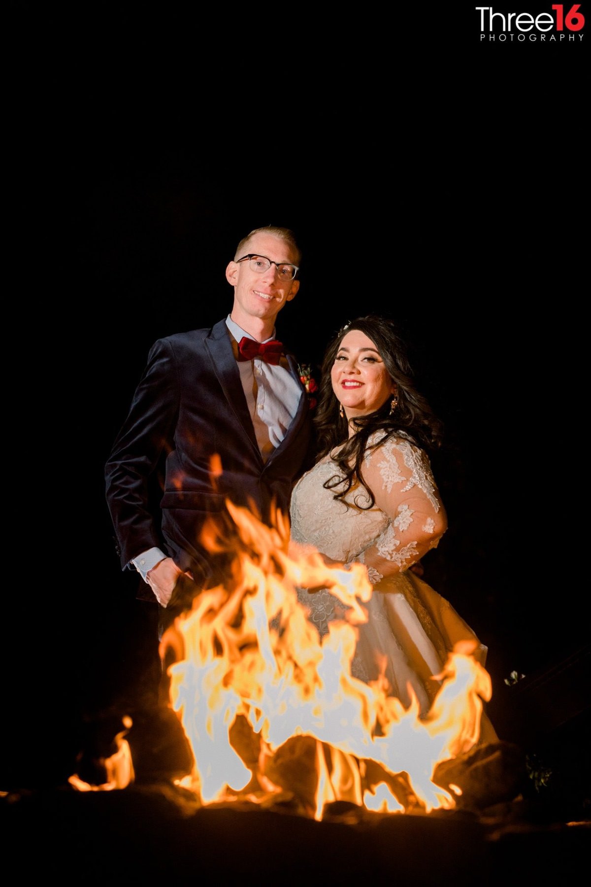 Bride and Groom pose behind a lit up fire pit