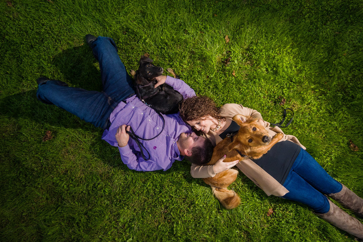 Engagement Photo of couple laying in grass with dogs