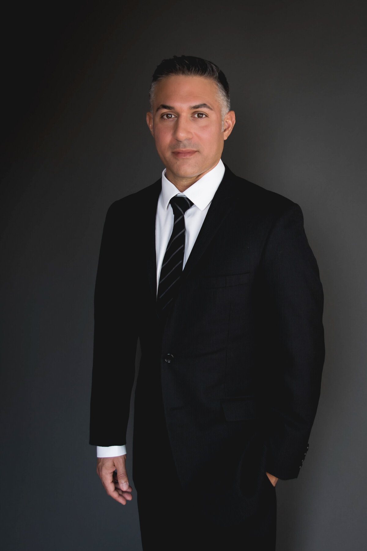 man  in business attire standing with hand in pocket looking at camera for business headshot