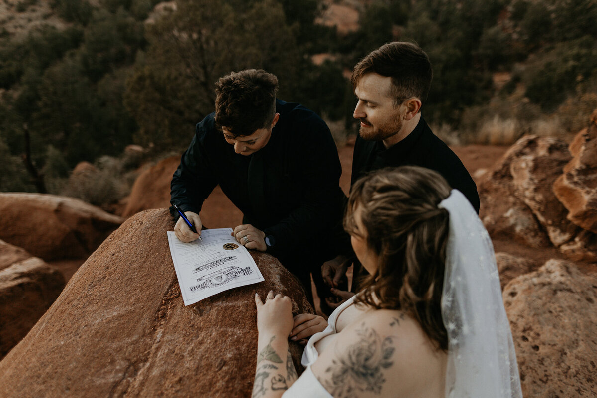 bride and groom signing their marriage license on a red rock in Colorado