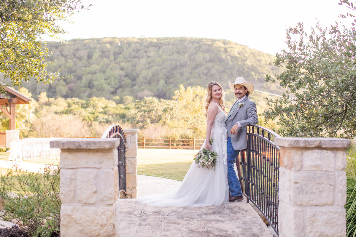 bride and groom stand on bridge at Boerne wedding with sunlight over hill