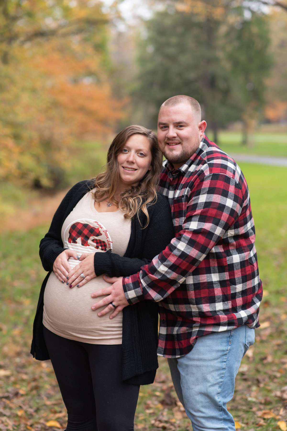 Husband & Pregnant Wife snuggled together in wooded area