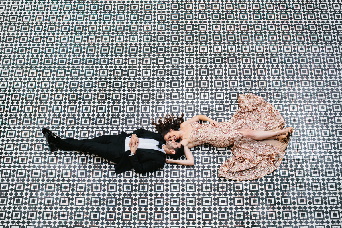 A couple in glamorous clothes laying on a black and white patterned tile photographed from above