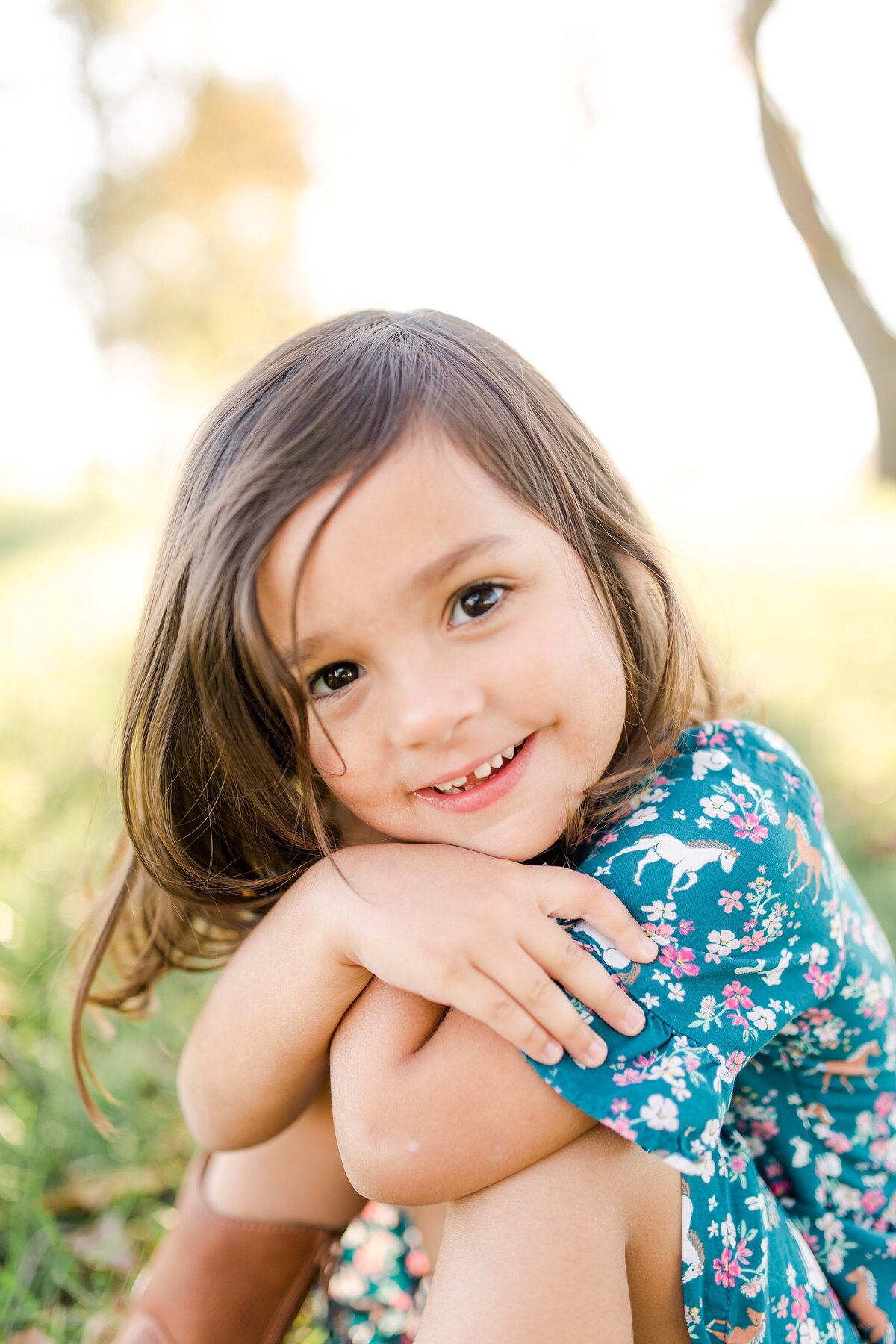 A little girl hugging her knees and smiling big while sitting in a field during a family session in Lexington KY.