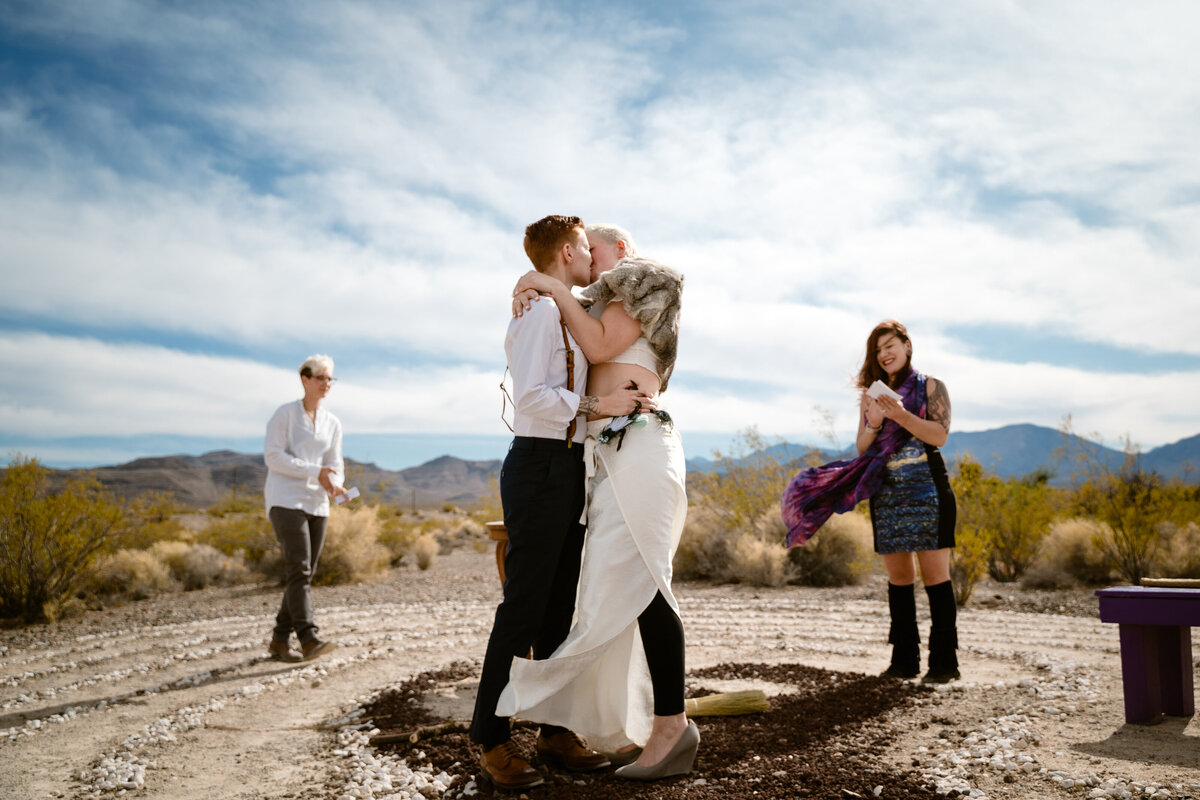 A couple kissing on top of a lookout with two guests around them.