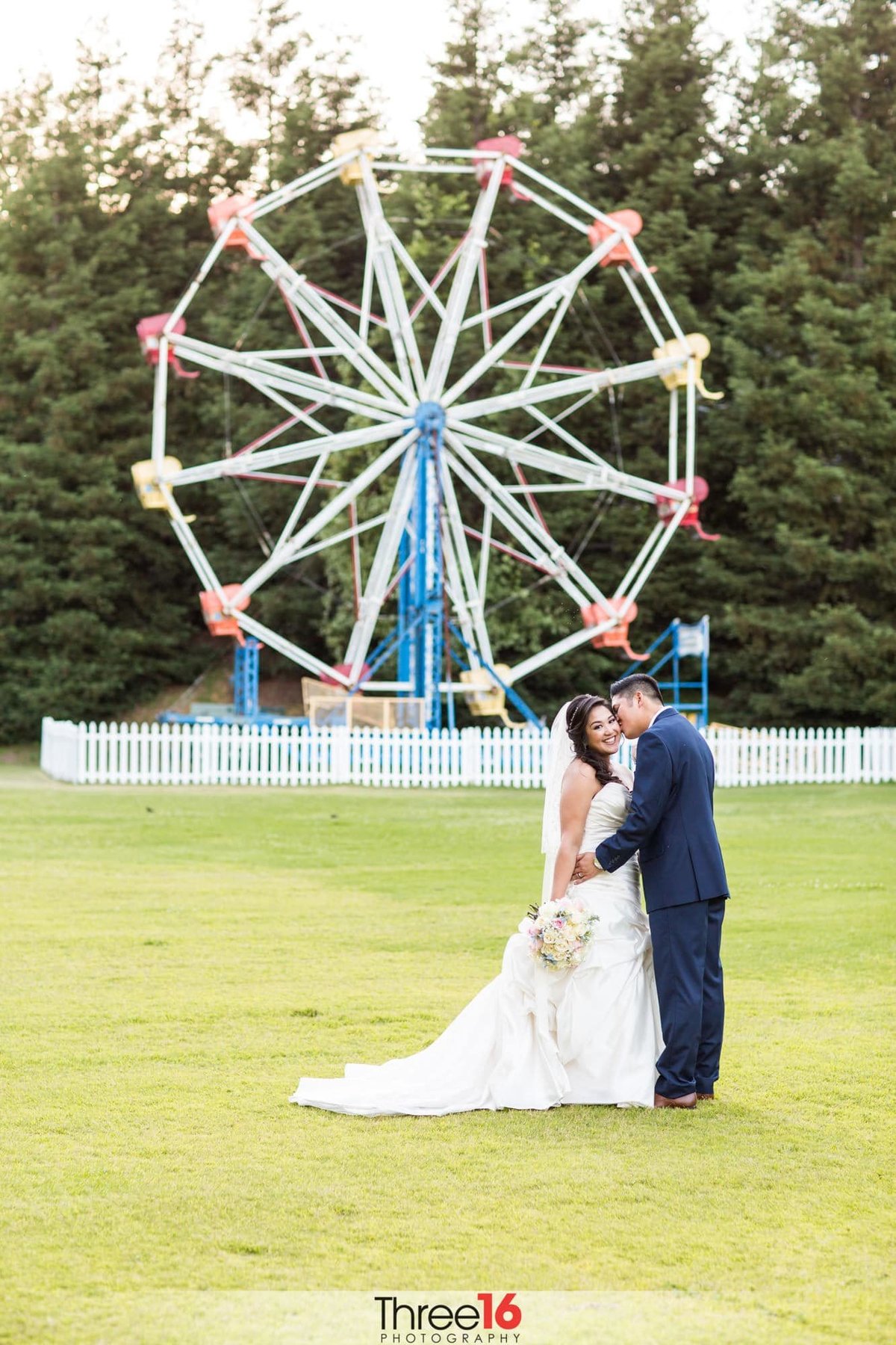 Groom kisses his Bride's cheek standing in front of the Ferris Wheel at Calamigos Ranch wedding venue in Malibu, CA