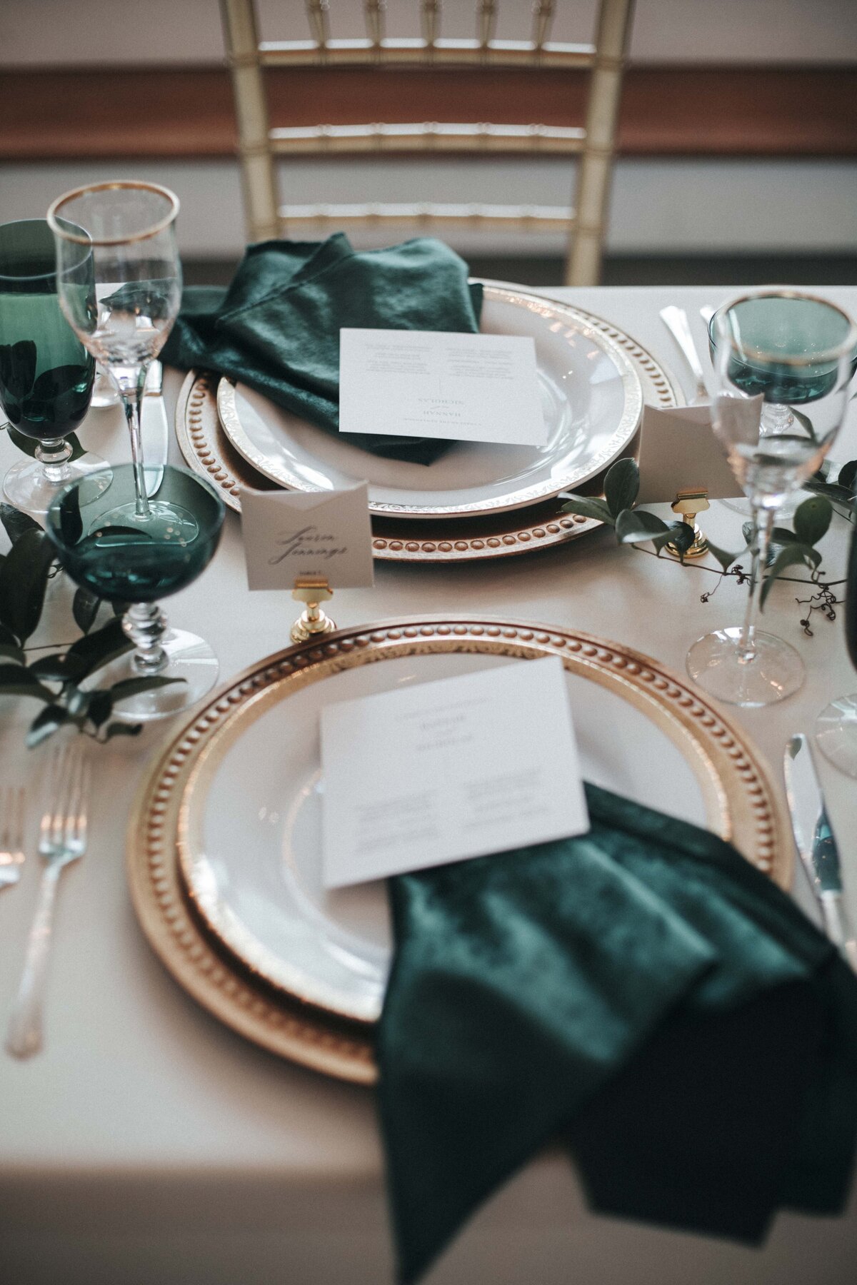 White squared place card with black font atop a dark green napkin and white plate.