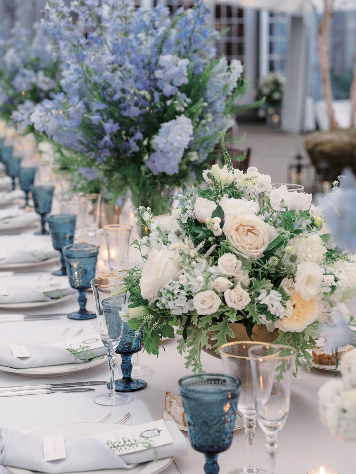 An elegant wedding dining table with white and blue flower centerpieces, cutleries, and blue wine glasses. Image by Jenny Fu Studio