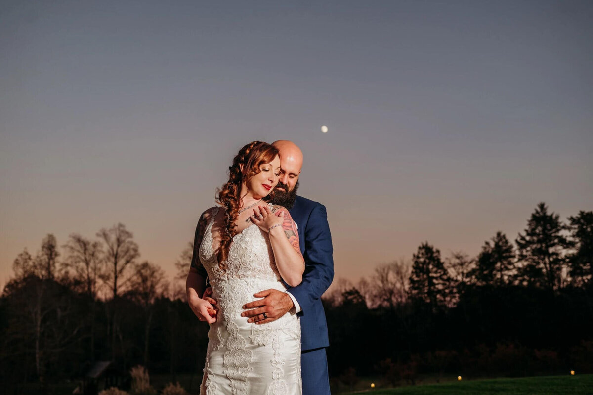 photo Of a groom hugging his bride's back with a full moon showing in the sky